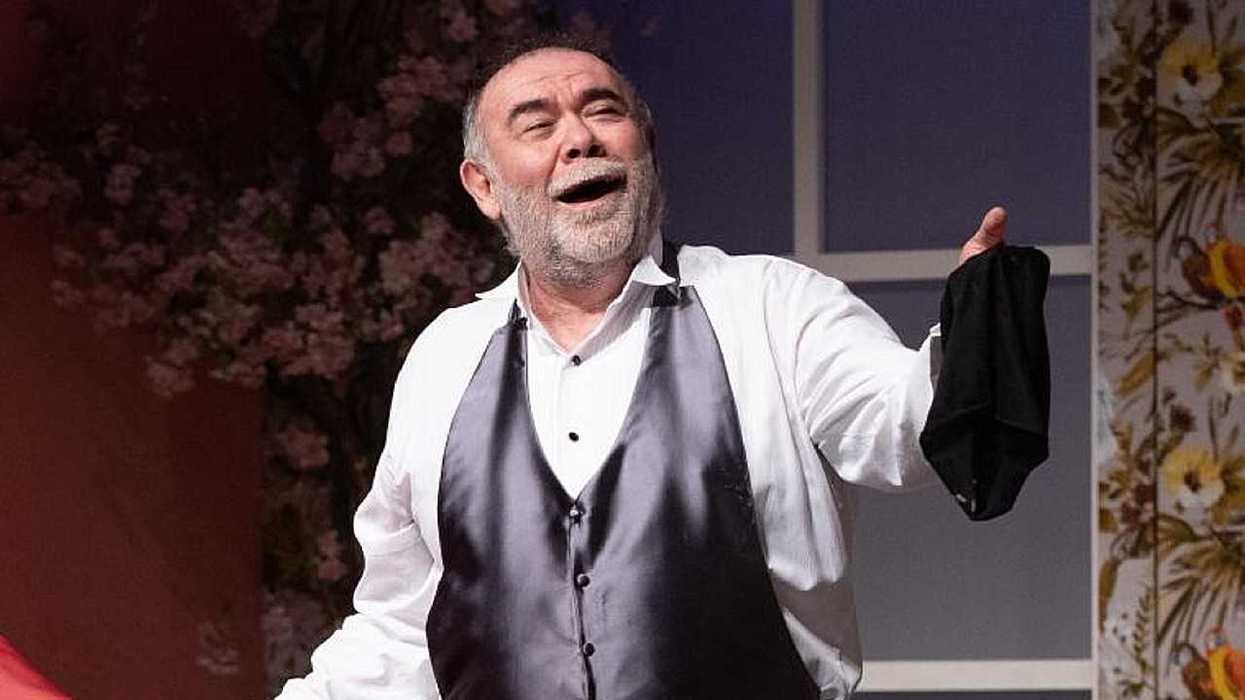 A bearded man in a waistcoat laughs onstage, holding up a black cloth.