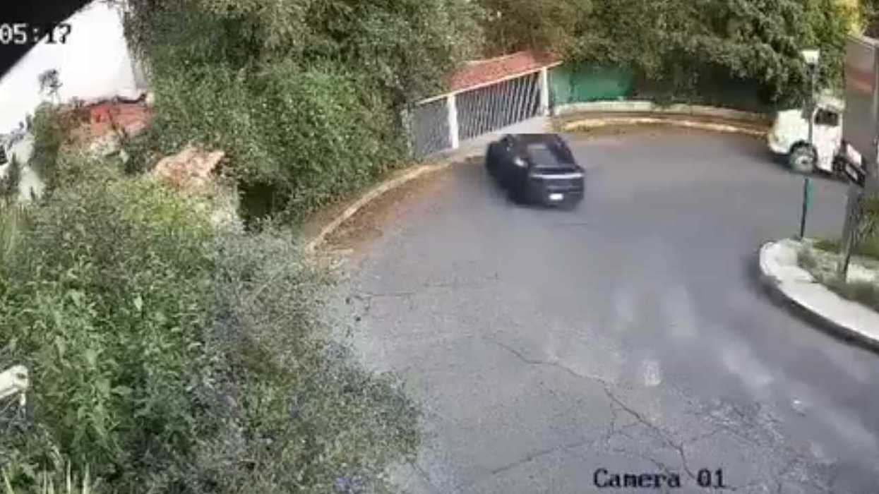 A black car turning on a curved, tree-lined road monitored by CCTV.