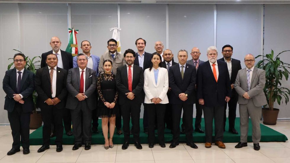 A group of 16 formally dressed people stands indoors, posing for a photo.