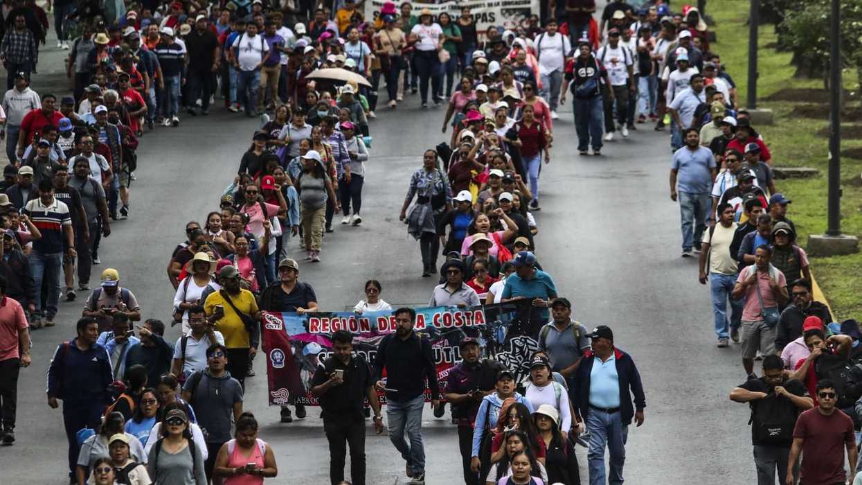 A large crowd of people marching on a street holding banners.