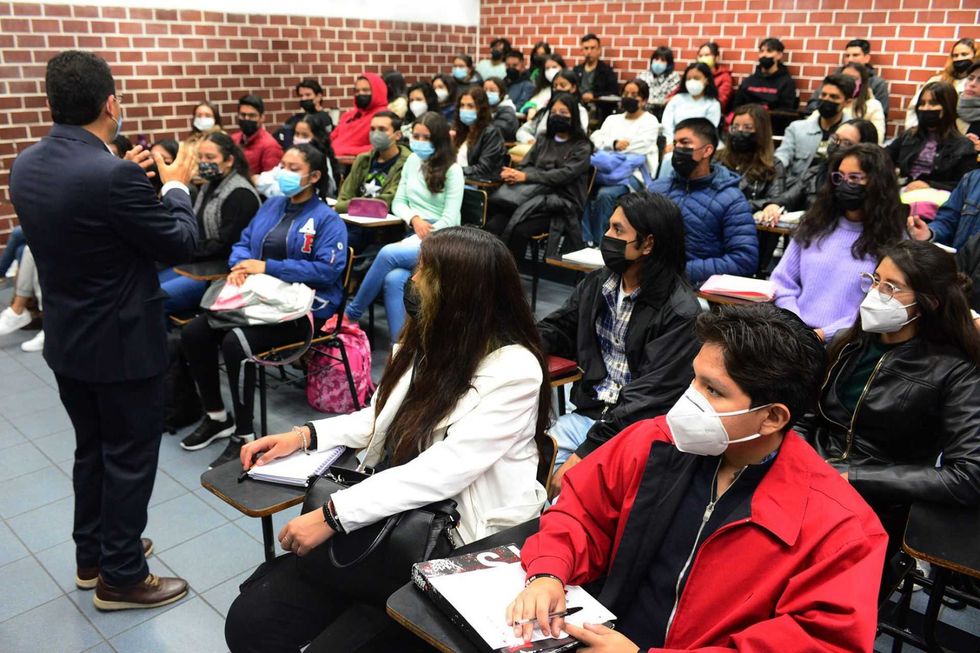 A lecturer speaks to a classroom full of masked students.