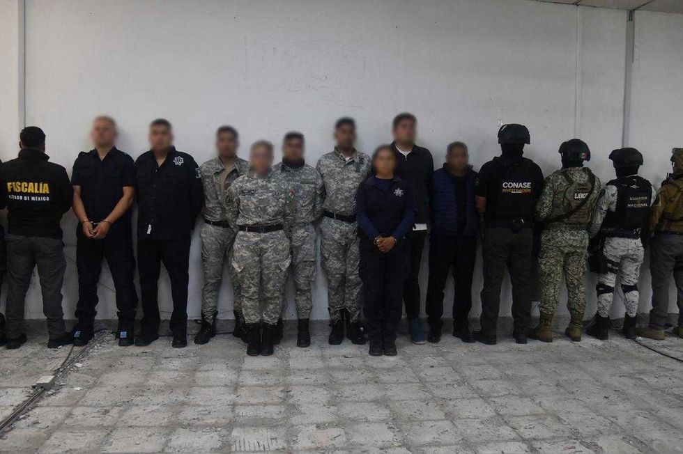 A line of people in varied uniforms against a plain wall indoors.