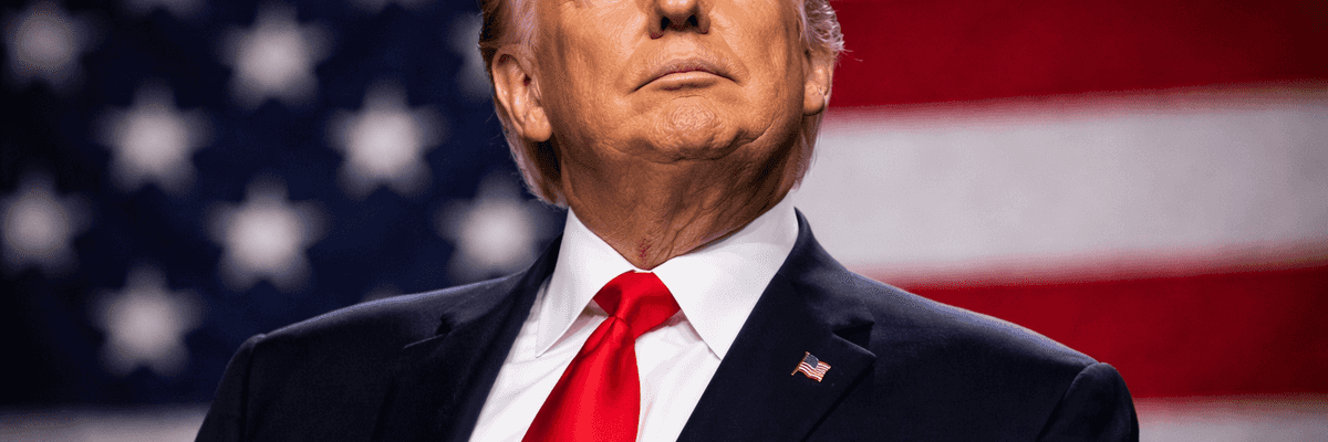 A person in a suit stands before an American flag, looking upwards confidently.