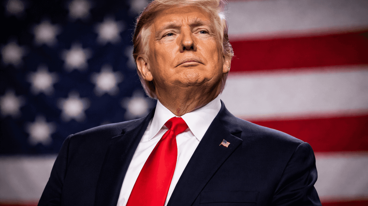 A person in a suit stands before an American flag, looking upwards confidently.