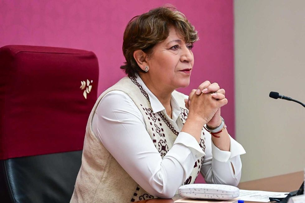 A person sits at a desk, hands clasped, with a microphone nearby.