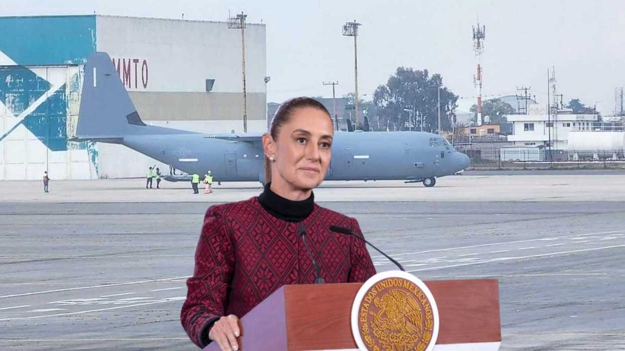 A person speaks at a podium near a military aircraft on an airfield.