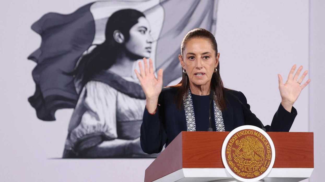A person speaks at a podium with a large portrait in the background.