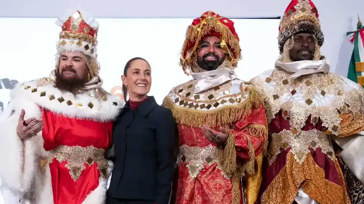 A person stands smiling with three individuals in ornate, colorful, kingly costumes.