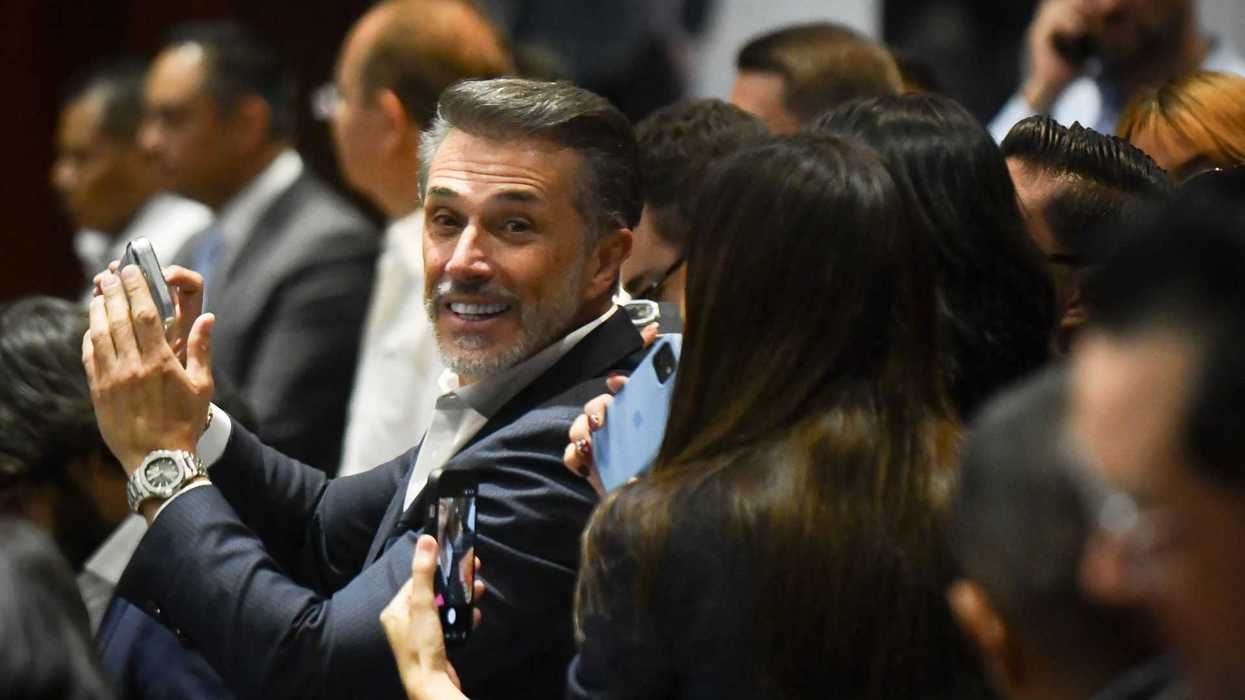A smiling man in a crowd claps, holding a smartphone.