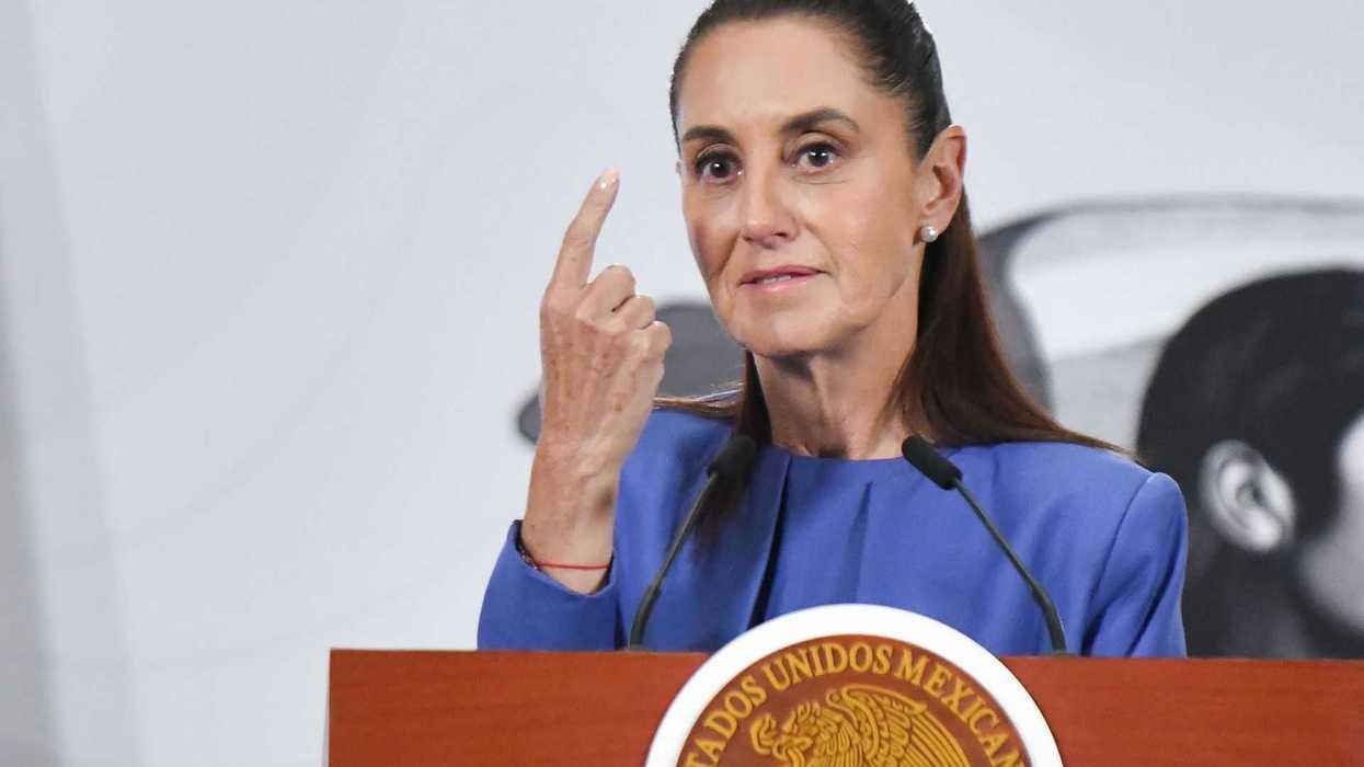 A woman speaks at a podium, gesturing and wearing a blue jacket.