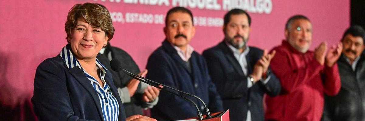 A woman speaks at a podium; several men clap behind her.
