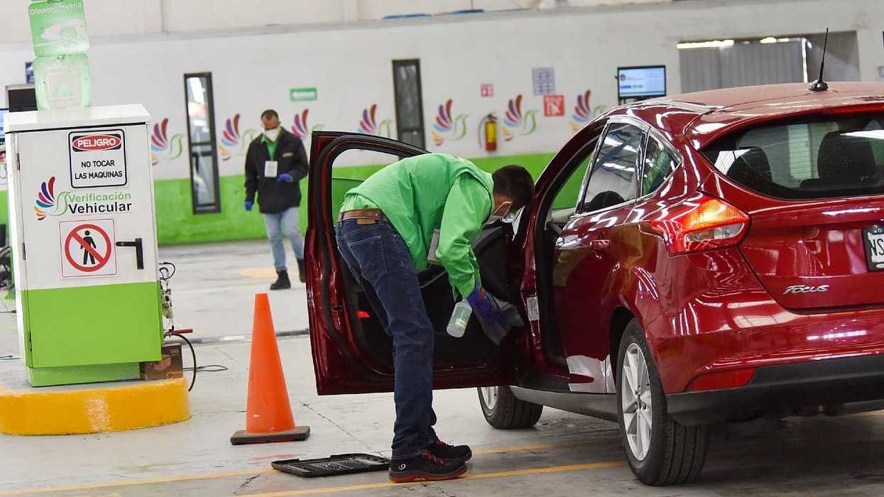 A worker inspects a red car during a vehicle emissions test.