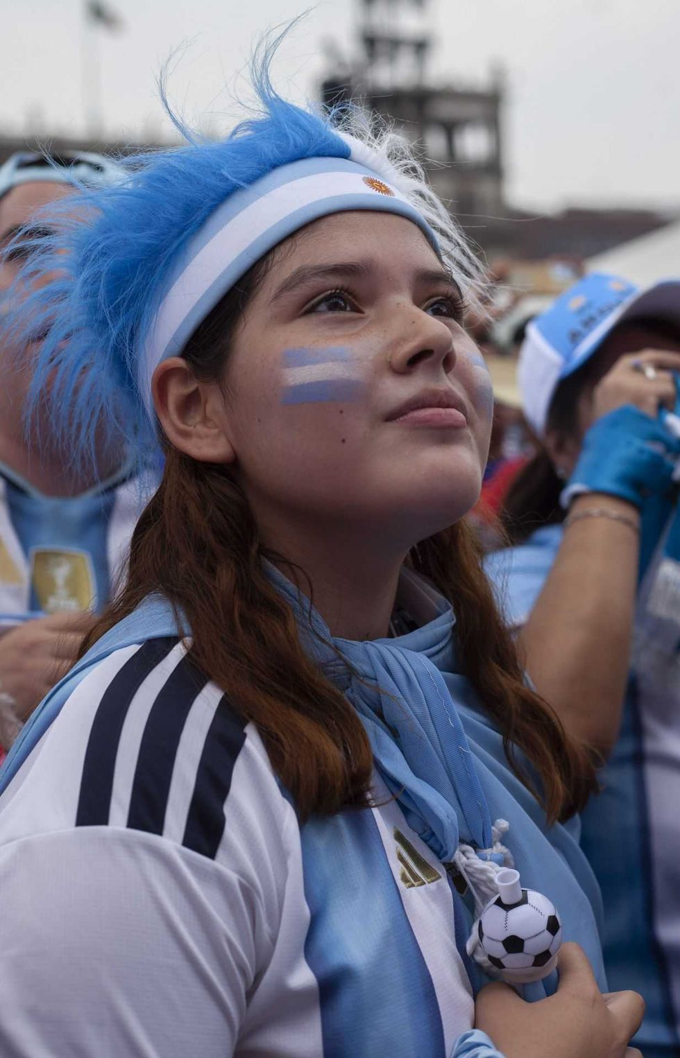 Argentina fan with face paint and blue headband, watching game intently.