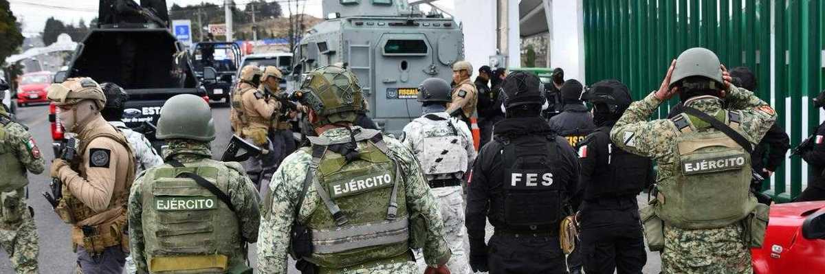 Armed military and police units gather near armored vehicles on a city street.