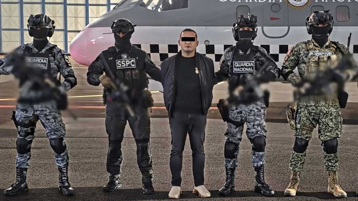 Armed officers escort a detainee in front of an aircraft with a "Guardia Nacional" logo.