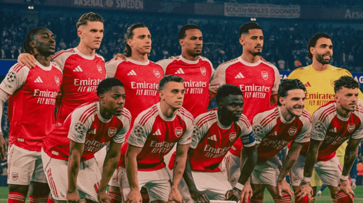 Arsenal soccer team poses in red jerseys before a match on the field.