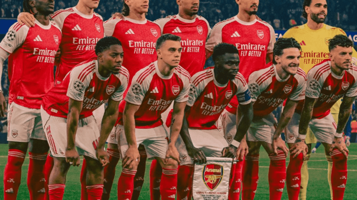 Arsenal soccer team poses in red jerseys before a match on the field.