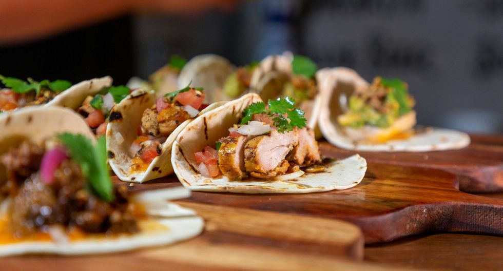 Assorted tacos with meat, cilantro, and salsa on wooden serving boards.
