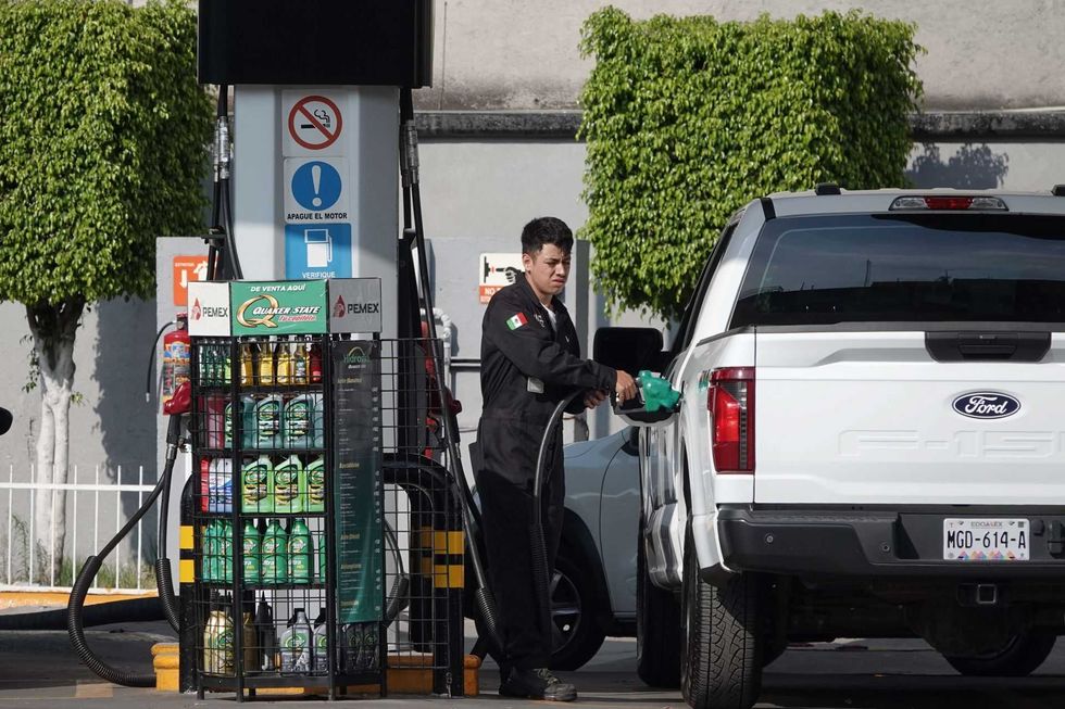Attendant refuels a white Ford truck at a gas station on a sunny day.