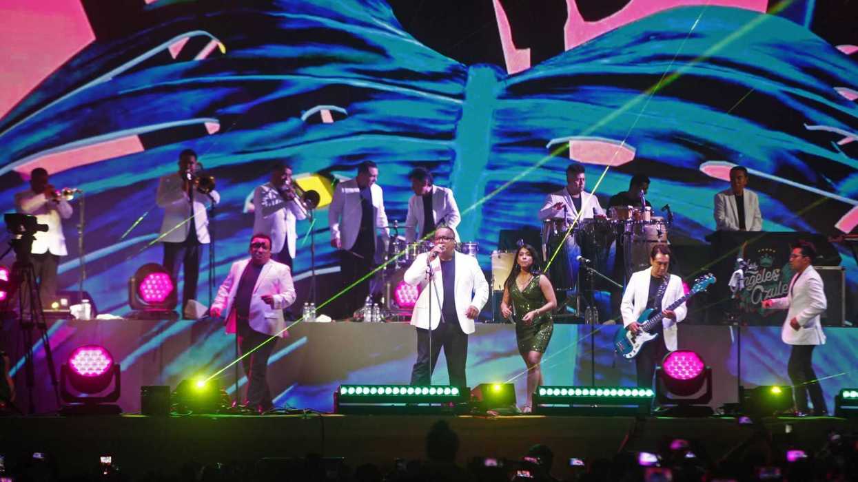 Band performing on stage with colorful backdrop and bright lights.