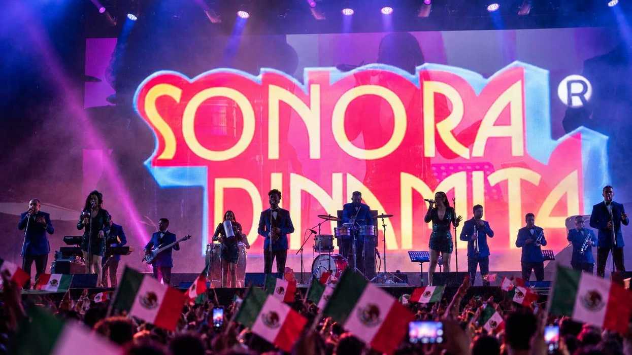 Band performing on stage with "Sonora Dinamita" sign, audience waving Mexican flags.