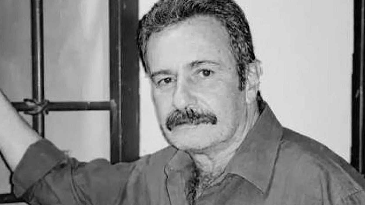Black and white photo of a man with a mustache by a window.
