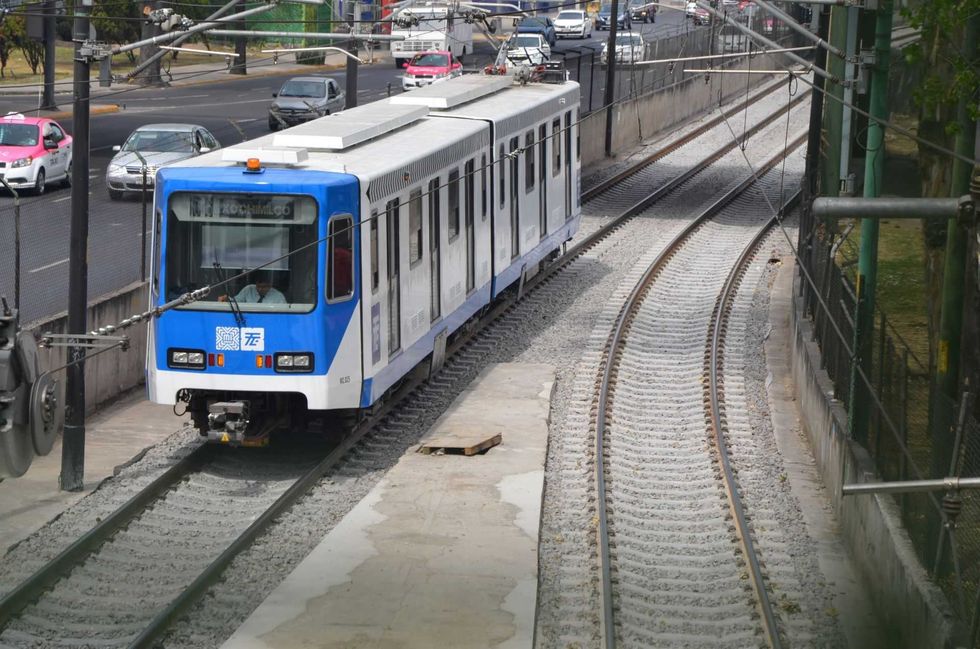 Blue and white tram on curved tracks beside busy road.