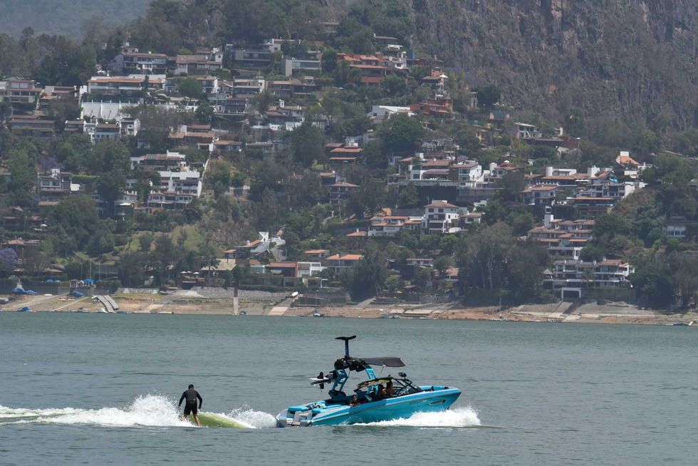 Boat and surfer on a lake with hillside houses in the background.