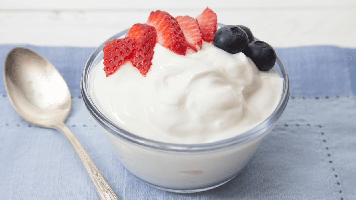 Bowl of yogurt topped with strawberries and blueberries on a blue napkin, spoon beside it.