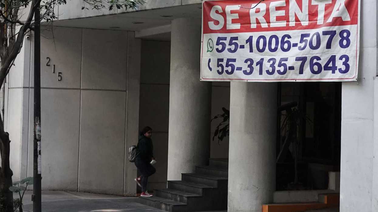 Building entrance with "Se Renta" sign and contact numbers, person entering step.