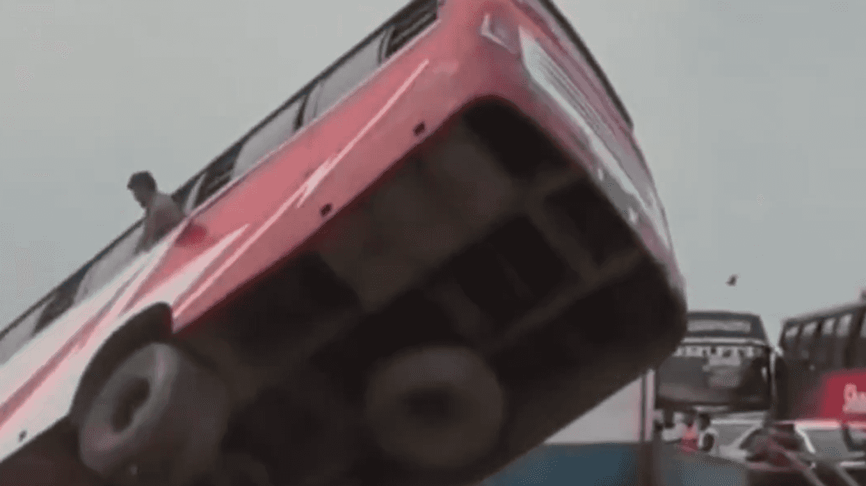 Bus tipping dangerously on a tilted platform, man standing beside.