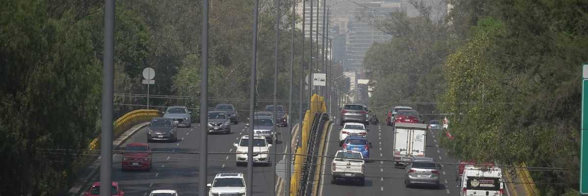 Busy highway with cars, buses, and trees lining both sides on a hazy day.