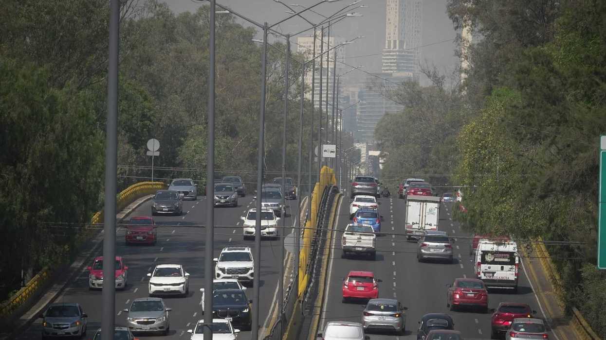 Busy highway with cars, buses, and trees lining both sides on a hazy day.