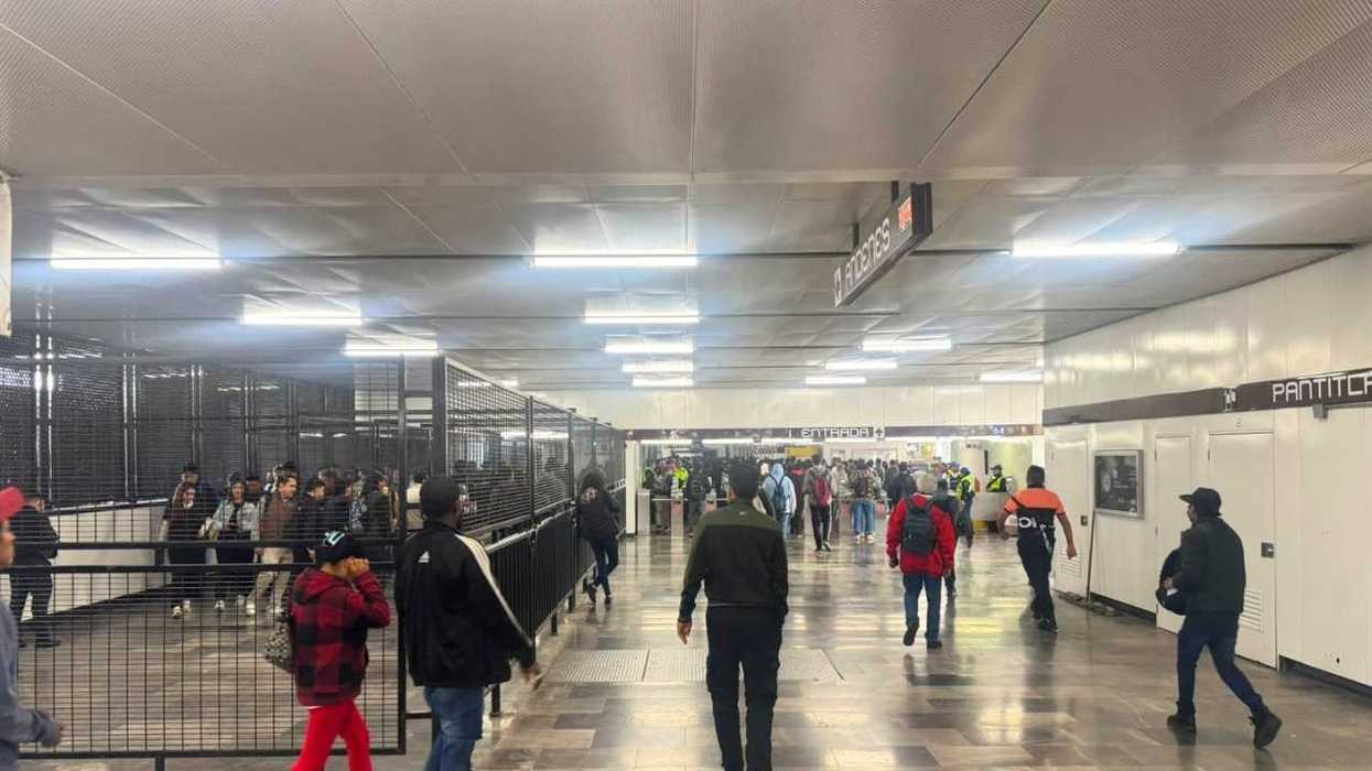 Busy subway station with people walking and signs overhead.