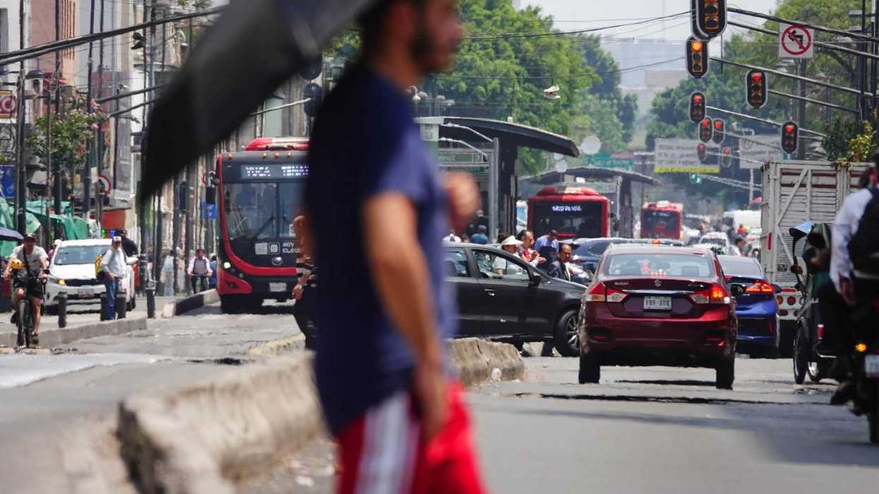 Busy urban street with traffic and pedestrians under an umbrella.