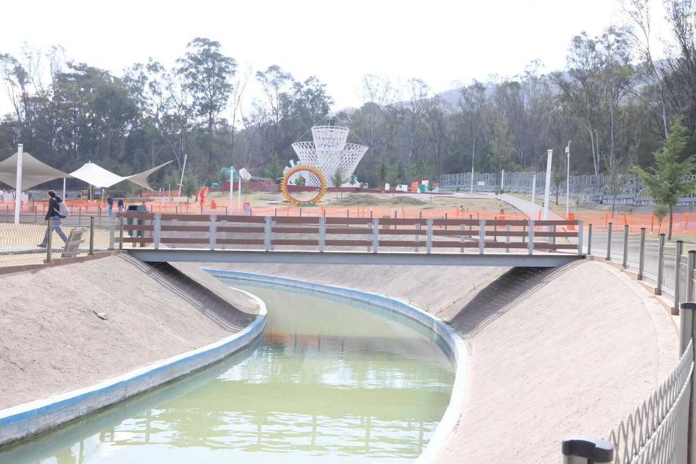 Canal and bridge in a park with sculptures and trees in the background.