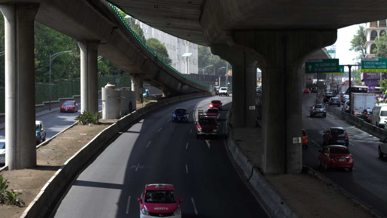 Cars driving on a multi-lane highway under a large overpass.