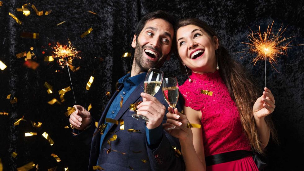 Cheerful couple with sparklers and champagne amid falling confetti, celebrating festively.