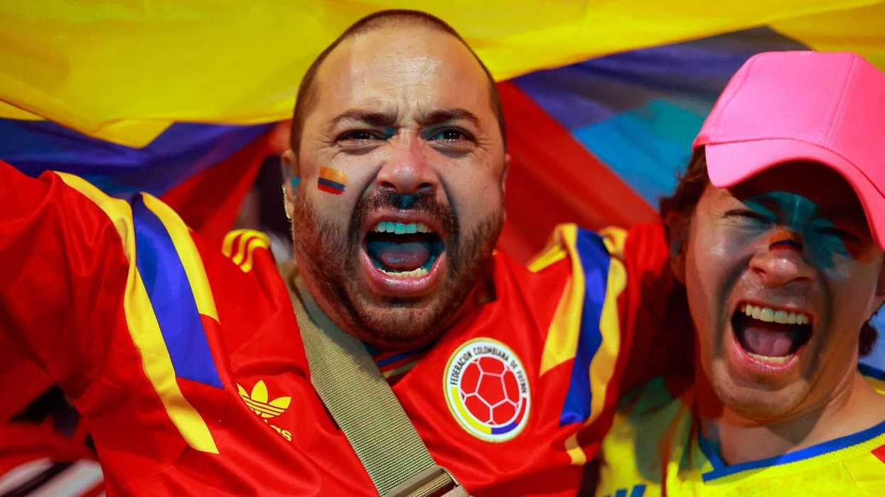 Cheering soccer fans in Colombian jerseys, vibrant flag in background.