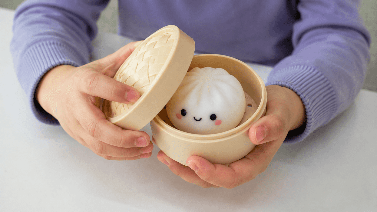 Child holding a cute, smiling bao toy in a bamboo steamer.