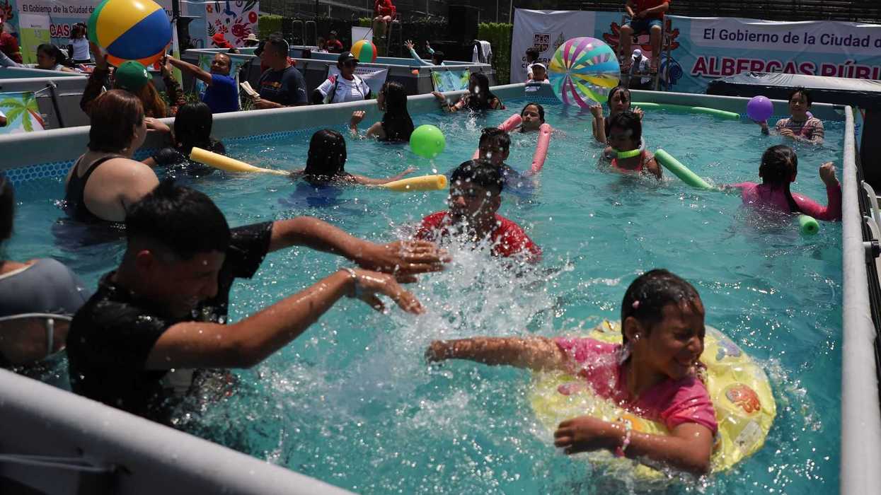 Children playing in a crowded public pool with colorful inflatables and a beach ball.