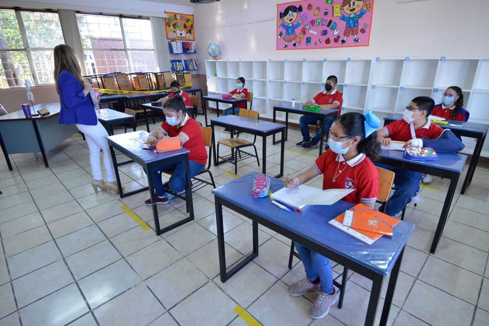 Classroom with socially distanced students in masks and a teacher standing.