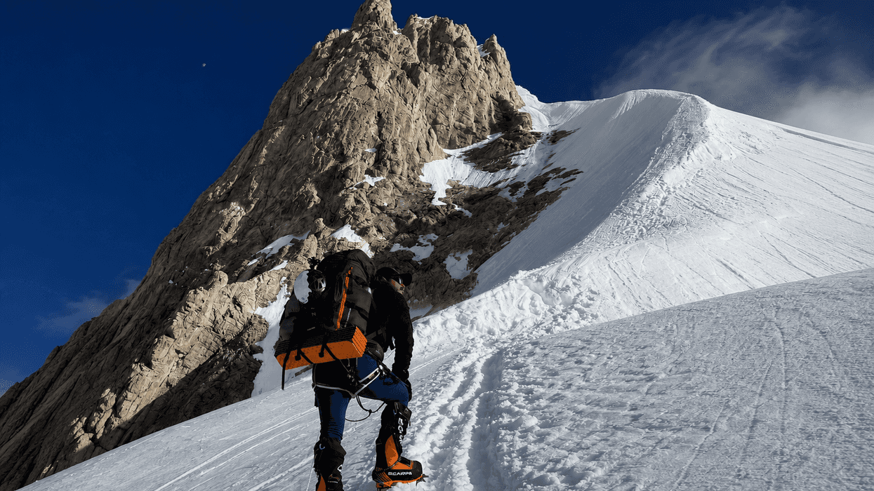 Climber ascending snowy mountain slope under a clear blue sky.