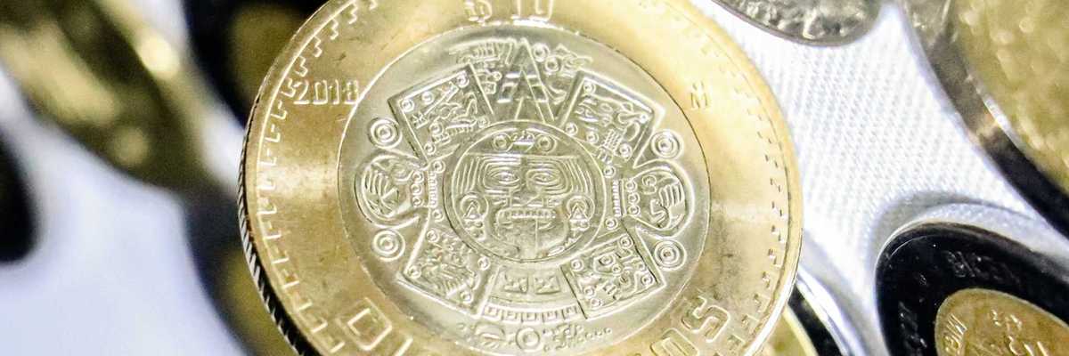 Close-up of a 10 pesos coin with intricate Aztec calendar design.
