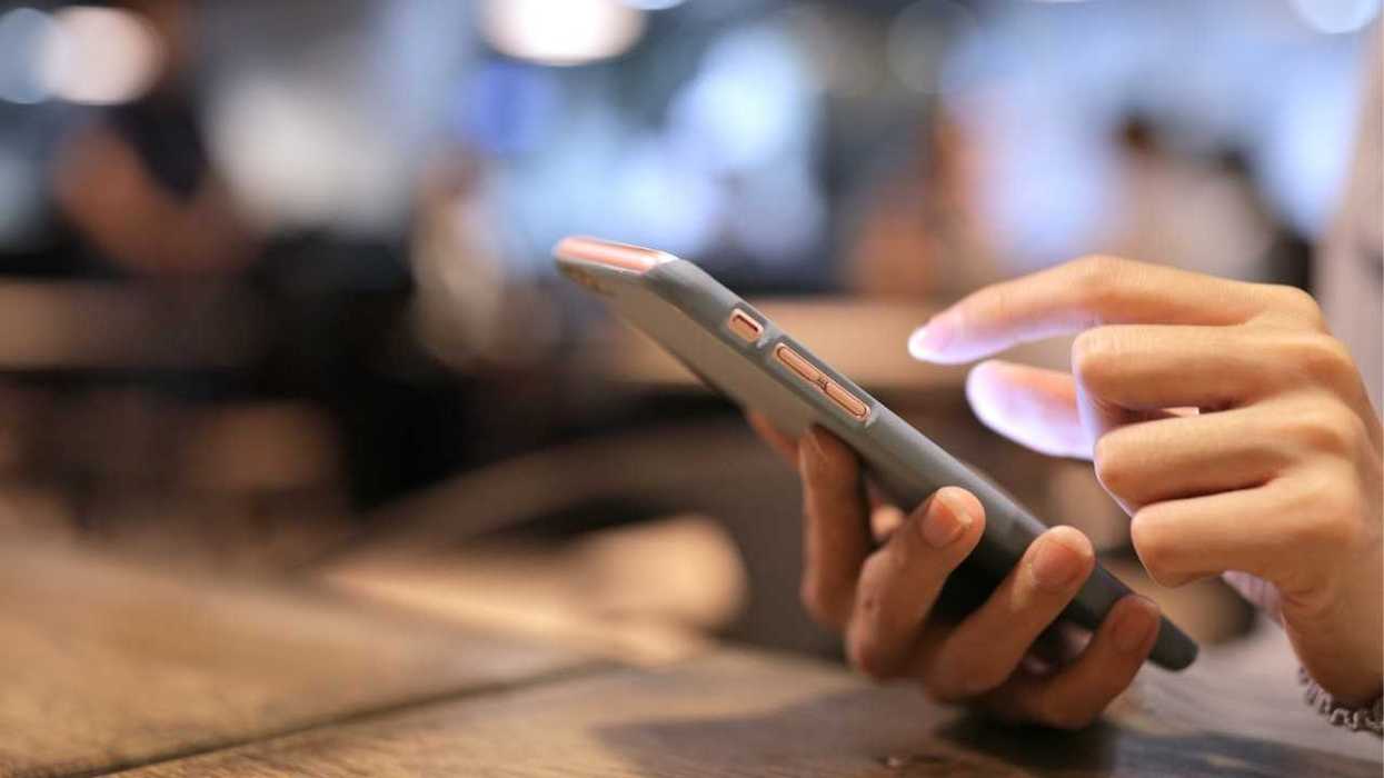 Close-up of hands using a smartphone in a dimly lit setting.
