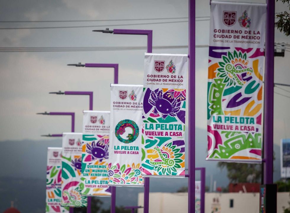 Colorful banners in Mexico City promote "La Pelota Vuelve a Casa" on purple poles.