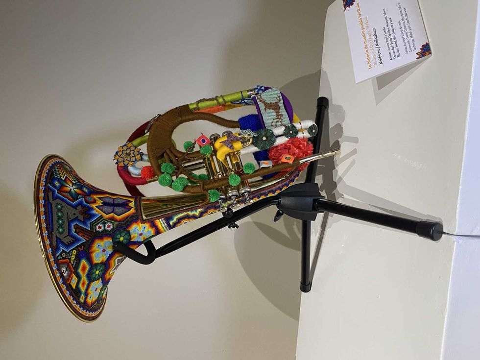 Colorful beaded tuba displayed on a stand with intricate patterns and vibrant designs.