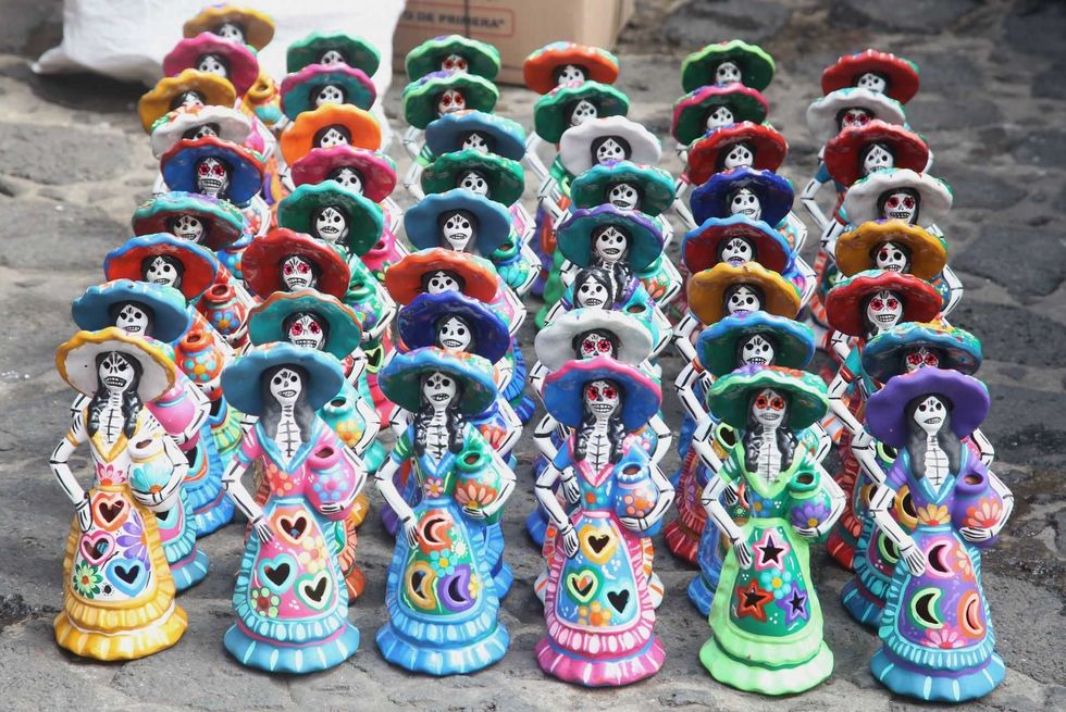 Colorful ceramic Catrina figures in rows, celebrating D\u00eda de los Muertos on cobblestones.