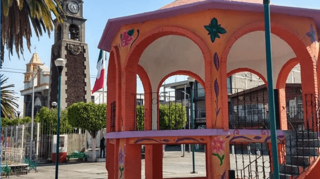Colorful gazebo in town square with clock tower and Mexican flag.