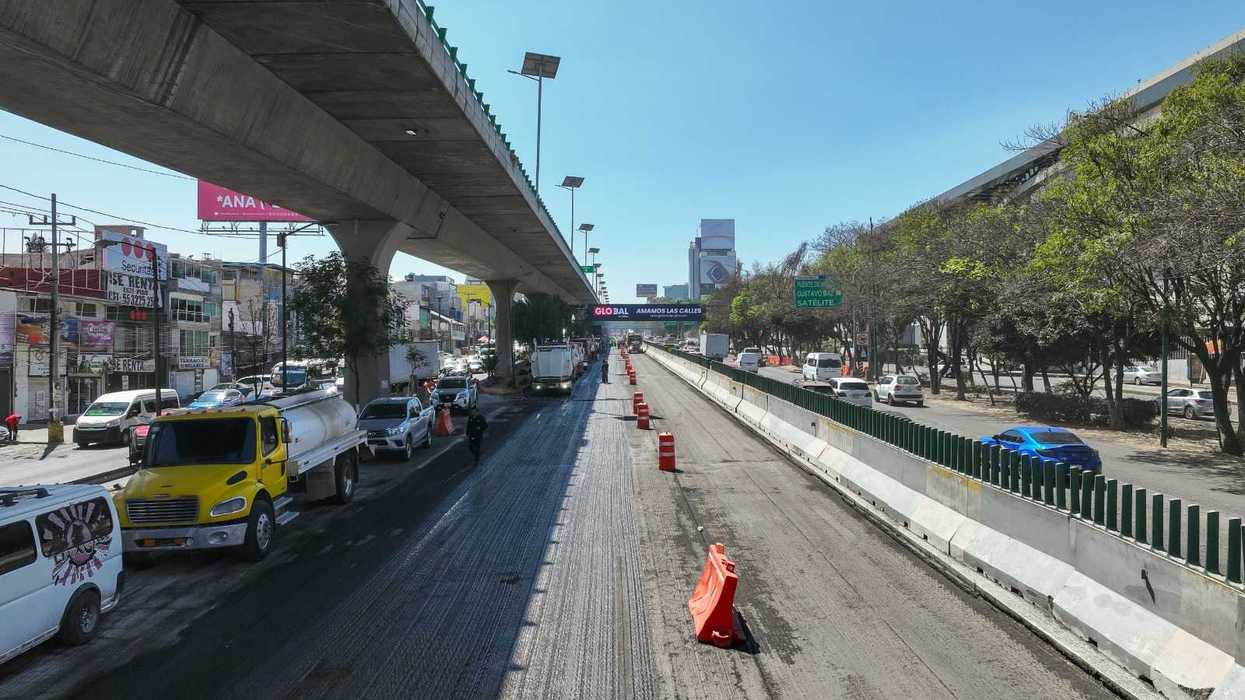 Construction on a multi-lane city road under a highway overpass, with traffic and orange cones.